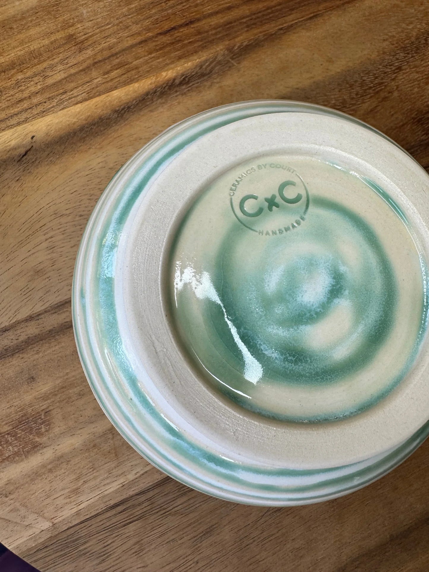 Handmade ceramic bowl with turquoise and white swirl glaze on wood table