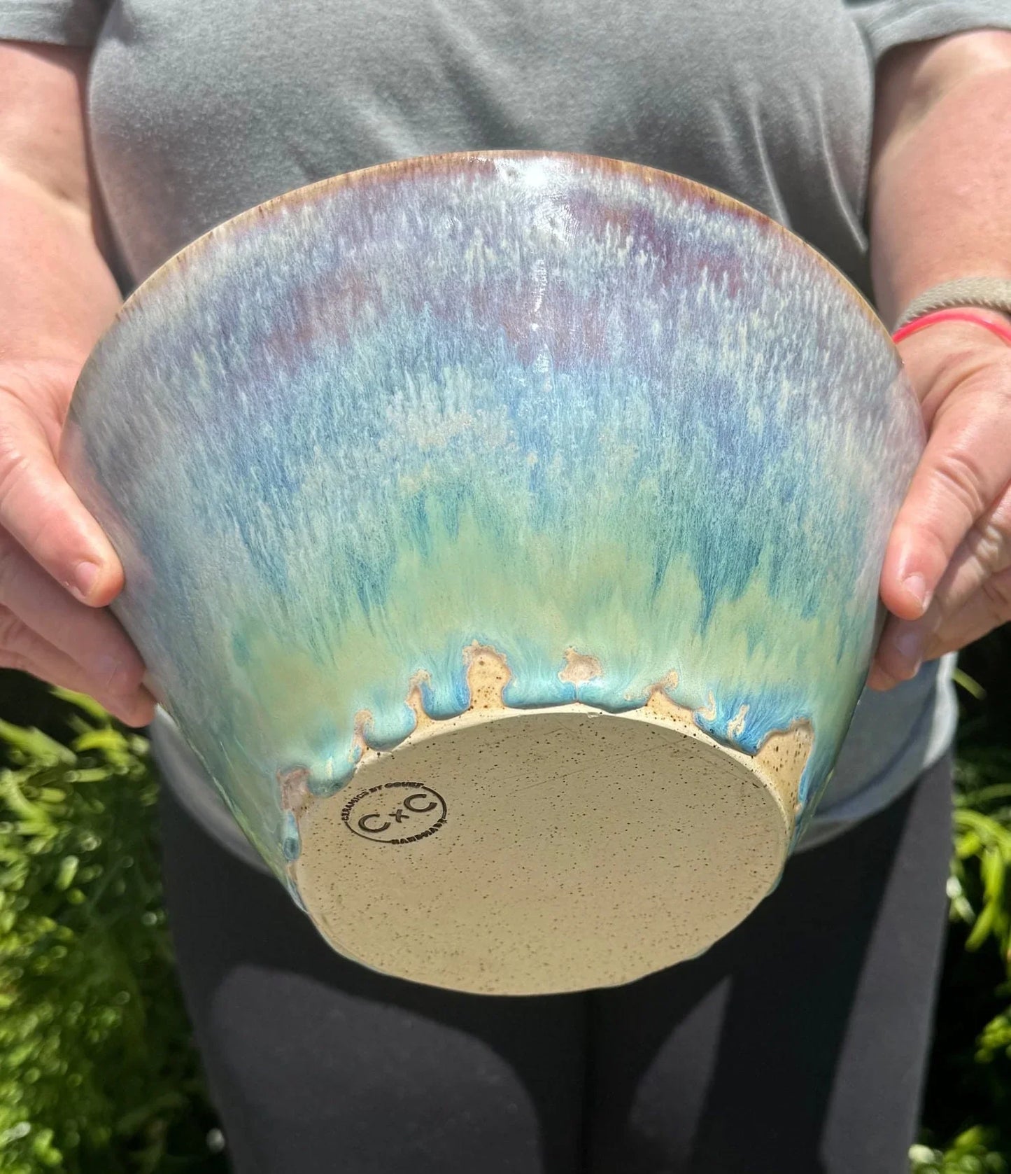 Hand holding a large blue and green glazed stoneware pottery bowl outdoors