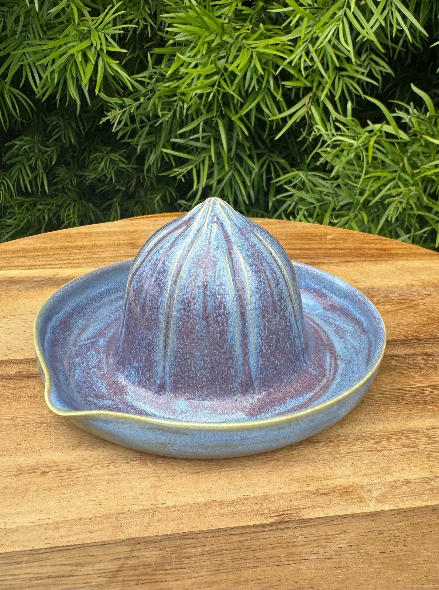 Handcrafted stoneware citrus juicer with blue and purple glaze on a wooden table