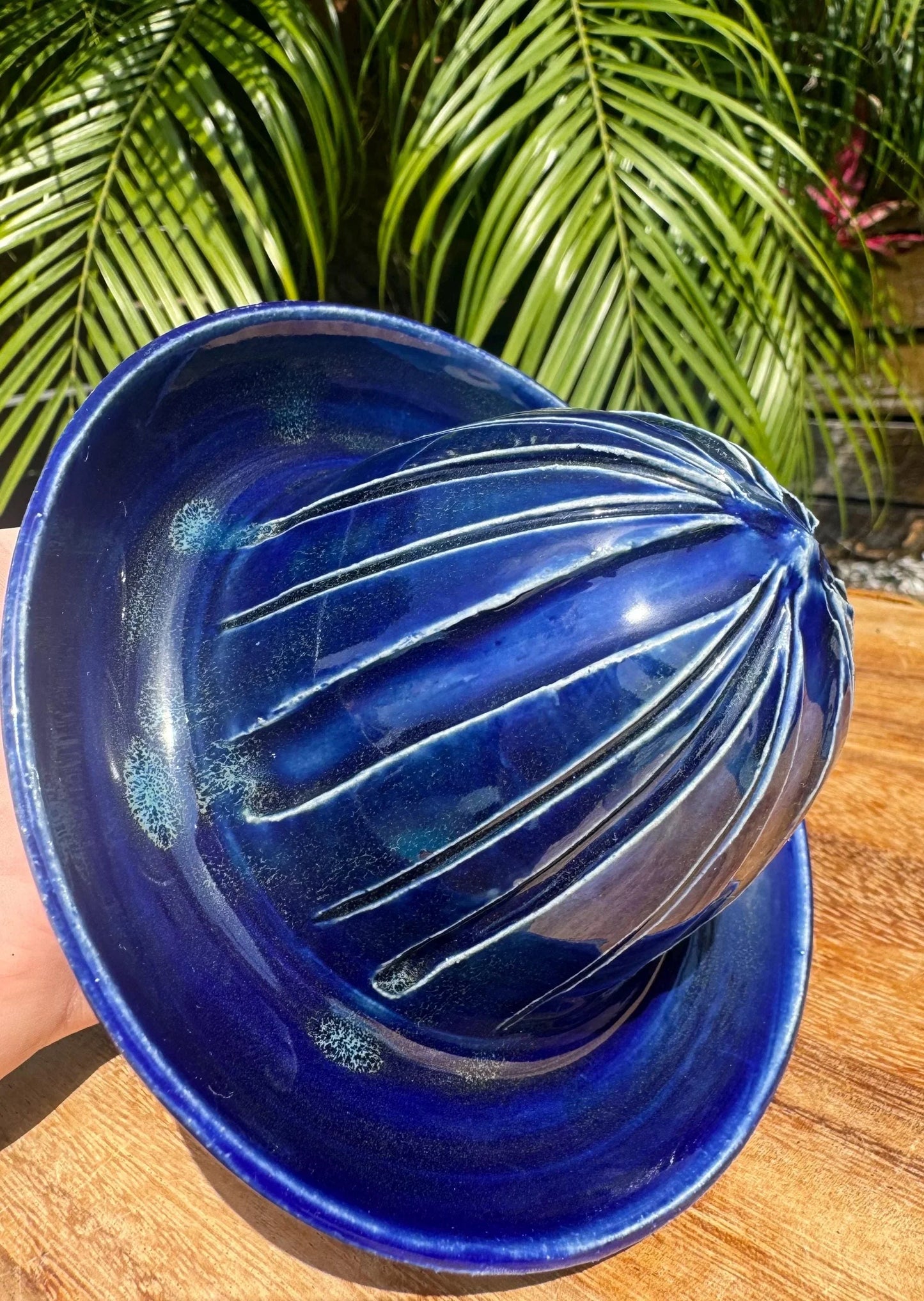 Handmade cobalt blue ceramic citrus juicer on wood with tropical leaves background