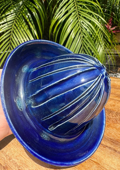 Handmade cobalt blue ceramic citrus juicer on wood with tropical leaves background
