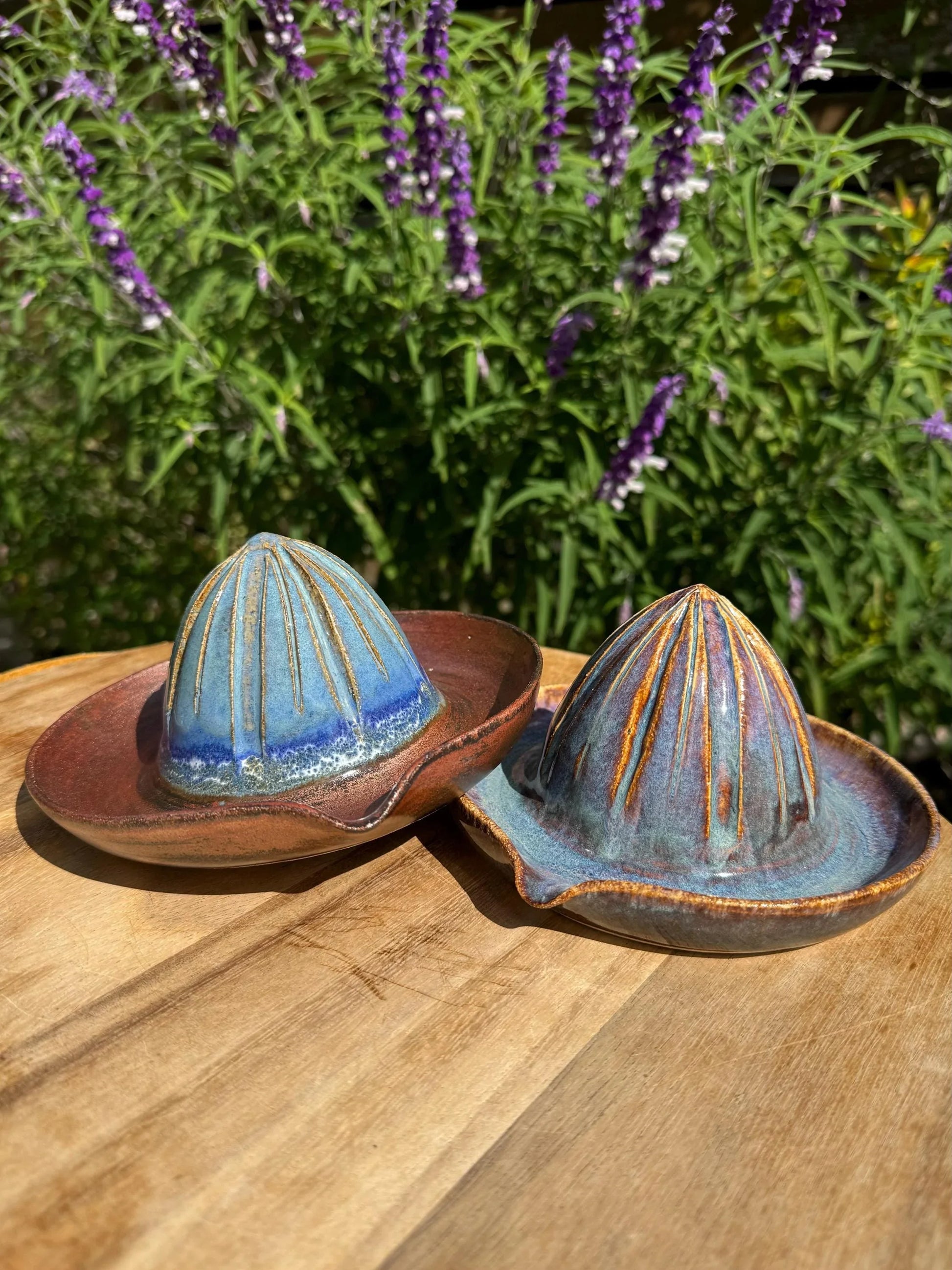 Handmade ceramic citrus juicers with blue and brown glaze on a wooden surface outdoors