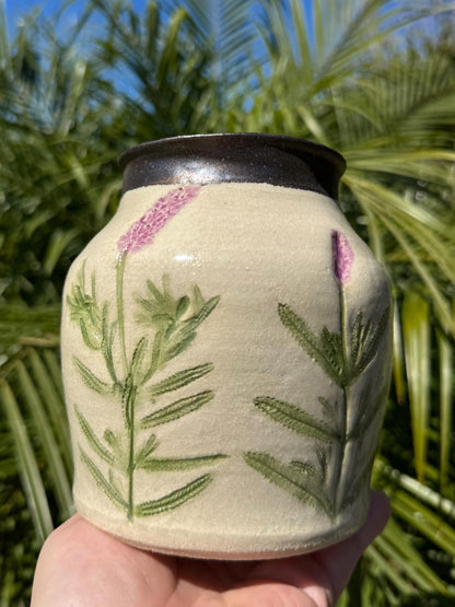 Handmade stoneware pottery vase with painted lavender flowers, held outdoors in sunlight.