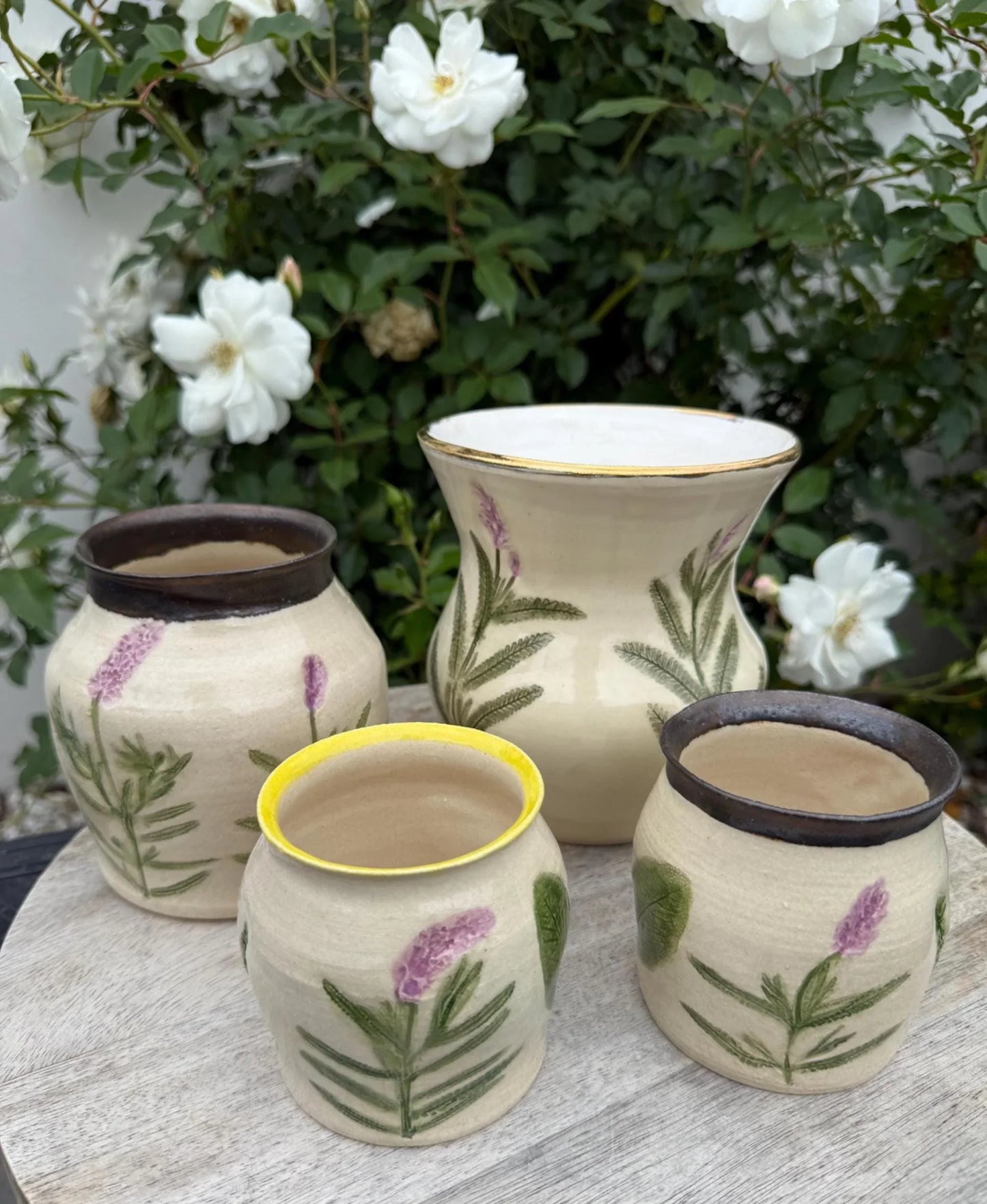 Handmade stoneware pottery set with floral designs, displayed outdoors near white roses.