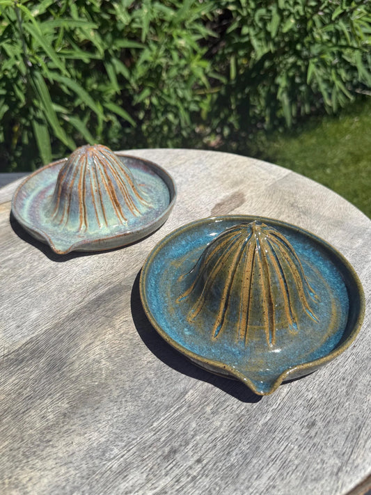 Handmade ceramic citrus juicers in blue and brown glaze on a wooden table outdoors.